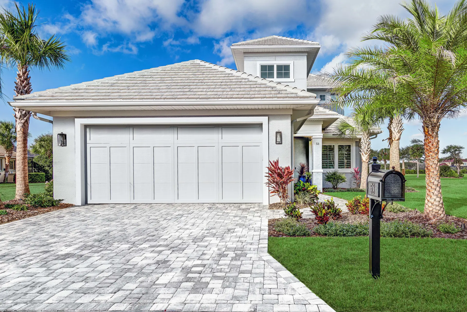Custom home garage elevation with paver driveway and landscaping